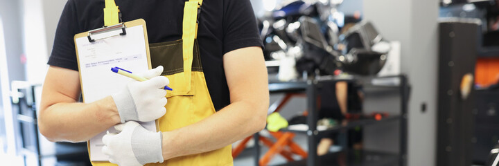 Auto mechanic locksmith in yellow uniform stands in car repair shop closeup