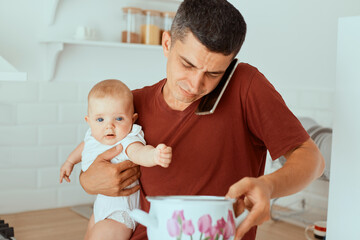 Horizontal shot of dark haired Caucasian young adult man wearing casual style t shirt holding baby...