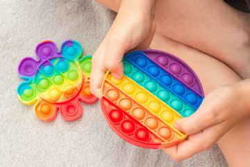 Top view on boy's hands playing with rainbow pop it fidget toy. Push bubble fidget sensory silicon stress relief toy. Antistress toy. Child mental health concept