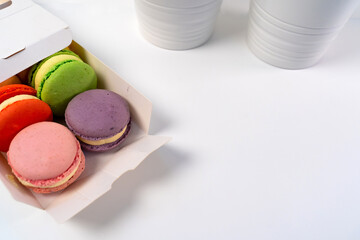 Opened Box of Macarons on a white table against the backdrop of a decorative flower in a pot.