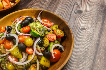 Healthy vegetable salad of fresh tomato, cucumber, onion, black olives,yellow sweet pepper with basil pesto sauce on wooden bowl.Top view, copy space. 