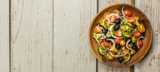 Healthy vegetable salad of fresh tomato, cucumber, onion, black olives,yellow sweet pepper with basil pesto sauce on wooden bowl.Top view, copy space. 