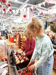 two cute girls are choosing Christmas tree decorations in the store, rejoicing and smiling, getting ready for Christmas and New Year. New Year's shopping, sale