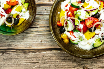 Fresh vegetable salad of fresh tomato, cucumber, onion, black olives,yellow sweet pepper with natural flavor yogurt sauce on ceramic bowl. It is located on an old natural wooden floor. Top view, copy 