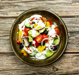 Fresh vegetable salad of fresh tomato, cucumber, onion, black olives,yellow sweet pepper with natural flavor yogurt sauce on ceramic bowl. It is located on an old natural wooden floor. Top view, copy 