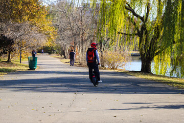 a man on an electric unicycle with a red helmet and a red backpack on a smooth footpath in the park...