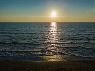 Drone view of a beautiful bright sunset on the sea with the reflection of a sunny path on the water, a piece of sandy beach is visible. Beautiful background of marine nature.