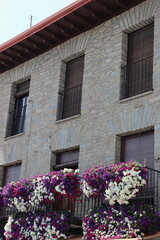 Fototapeta na wymiar Close-up of a stone house with a railing, wooden blinds and geranium flowers decorating the balconies in Villafranca do Bierzo, León. Vertical image.