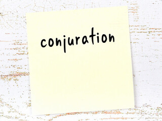 Yellow sticky note on wooden wall with handwritten word conjuration