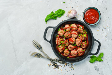 Meatballs in sweet and sour tomato sauce in a frying pan. Top view. On a stone background.