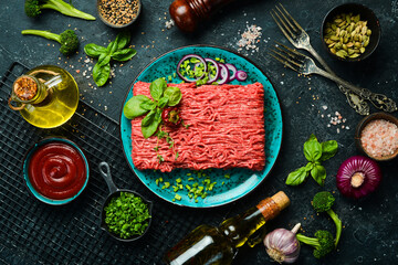 Raw mince beef, ground meat with herbs and spices on a plate. Top view. On a stone background.