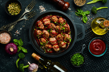Meatballs in sweet and sour tomato sauce in a frying pan. Top view. On a stone background.
