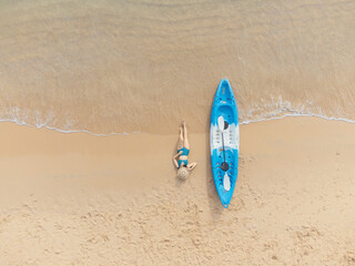 Beautiful woman in bikini lying on the beach with a kayak beside - Powered by Adobe