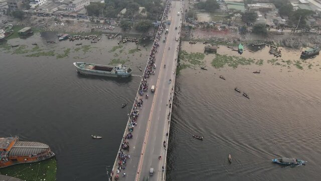 drone rotating view over busy bridge on Buriganga river, Dhaka, Bangladesh, and wooden steamers at riverbank. Fast motion