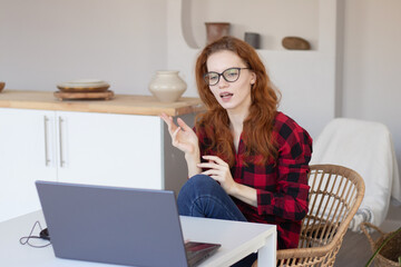 young pretty red-haired girl talking using a computer at home in the kitchen