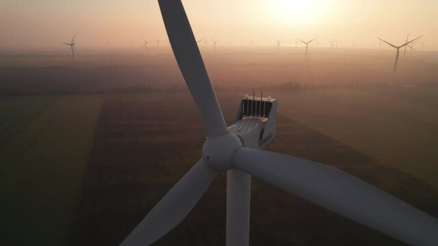 Close-up of wind turbine blades at sunset or sunrise. Windmills with rotating wings among green fields. Technology for wind energy, renewable energy source, earth care. Wind power station, drone video