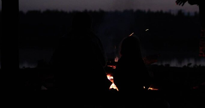 family next to a fire on the background of a lake at night