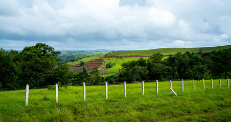 Landscape with green field and fenced area under cloudy sky in Mondulkiri province in Cambodia