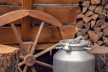 Old vintage milk churns. Aluminium Can for milk or water. Wooden Cart and logs as background
