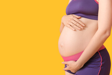 Sporty young pregnant woman on yellow background