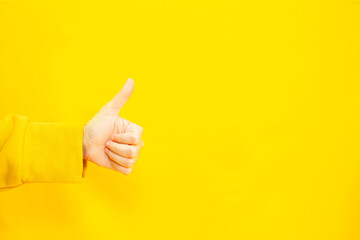 woman's hand with thumbs up gesture  in copy space area for advertisement promotion or text on a yellow background