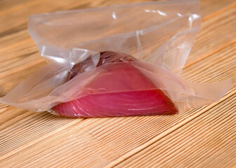 A piece of tuna in a vacuum package on a wooden background. No people, blurred background