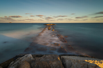 Coastal breakwater overflown with water during high tide at sunset