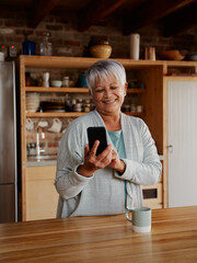 Portrait orientation of happy multi-cultural elderly female typing a message on smartphone while...