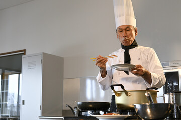 飲食店の厨房でコック服を着たシニア男性が料理を作る