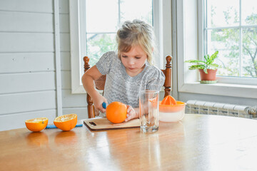 the child girl in the kitchen cuts and squeezes oranges juice