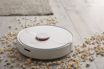 Modern robot vacuum cleaner with scattered popcorn on floor in room