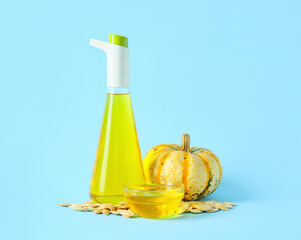 Jug and bowl of tasty pumpkin seed oil on blue background
