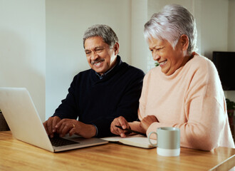 Multi-cultural elderly couple smiling at family on online call. Sitting at modern kitchen counter with laptop.
