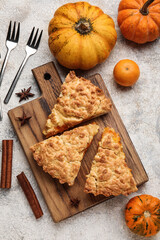 Wooden board with pieces of tasty pumpkin pie on grey background