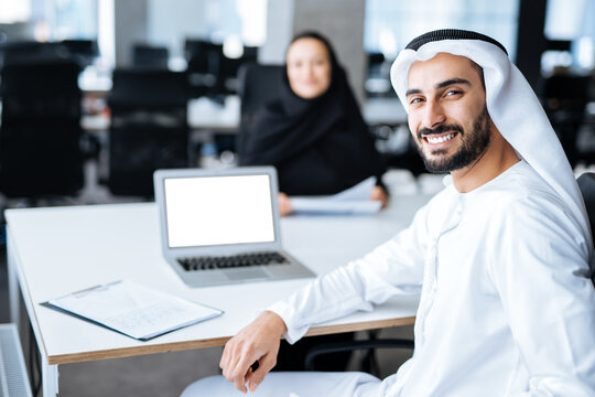 Man and woman with traditional clothes working in a business office of Dubai. Portraits of successful entrepreneurs businessman and businesswoman in formal emirates outfits. Concept about middle east