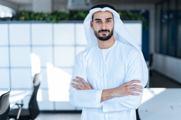Handsome man with dish dasha working in his business office of Dubai. Portraits of a successful businessman in traditional emirates white dress. Concept about middle eastern cultures - obrazy, fototapety, plakaty