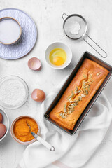 Baking dish with tasty pumpkin pie and ingredients on light background