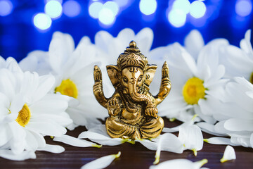 Golden lord ganesha sculpture in daisy flowers over blue illuminated background. Celebrate lord ganesha festival