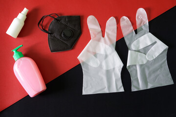 Protective medical gloves with victory sign, respirator, detergent dispenser and disinfectant spray on a black and red background. The concept of defeating the covid-19 virus and recovering