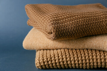 Stack of soft modern sweaters on dark background, closeup