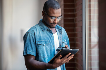 Confident businessman working with digital tablet while standing near windows in a coworking space.
