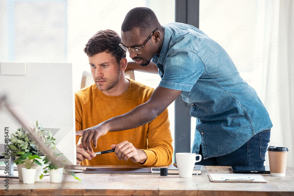 Poster graphic designer working with computer while showing his job to his colleague in modern startup offi