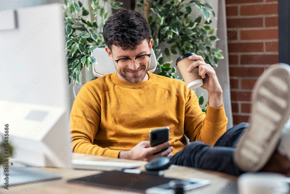 Poster graphic designer working with computer while using smartphone and drinking coffee in modern startup 