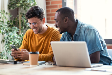 Two graphic designer taking a break while looking funny things in mobile phone together in modern...