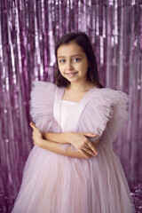 beautiful girl with big eyes in a pink dress stands against the background of New Year tinsel