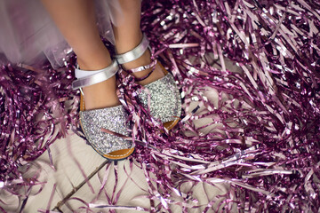 legs of a girl in shiny shoes on a pink tinsel background on birthday holiday