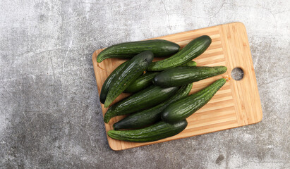 Fresh small cucumbers on a rectangular cutting wooden board on a dark grey background. Top view, flat lay