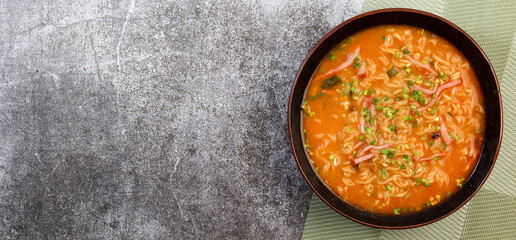 Instant noodles with sausage and green onions in a bowl on a dark grey background. Top view, flat lay