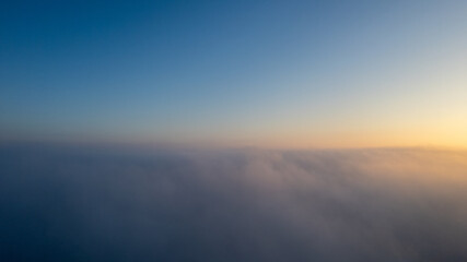 Aerial View. Flying in fog, fly in mist over the early morning clouds in the rising sun. Aerial camera shot. Flight above the clouds towards the sun with the mist clouds floating by. Misty weather