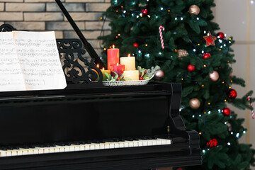 Grand piano with note sheets and burning candles in room decorated for Christmas